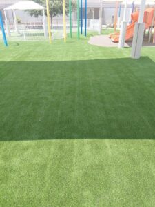 Open synthetic turf field beside colorful playground shade poles